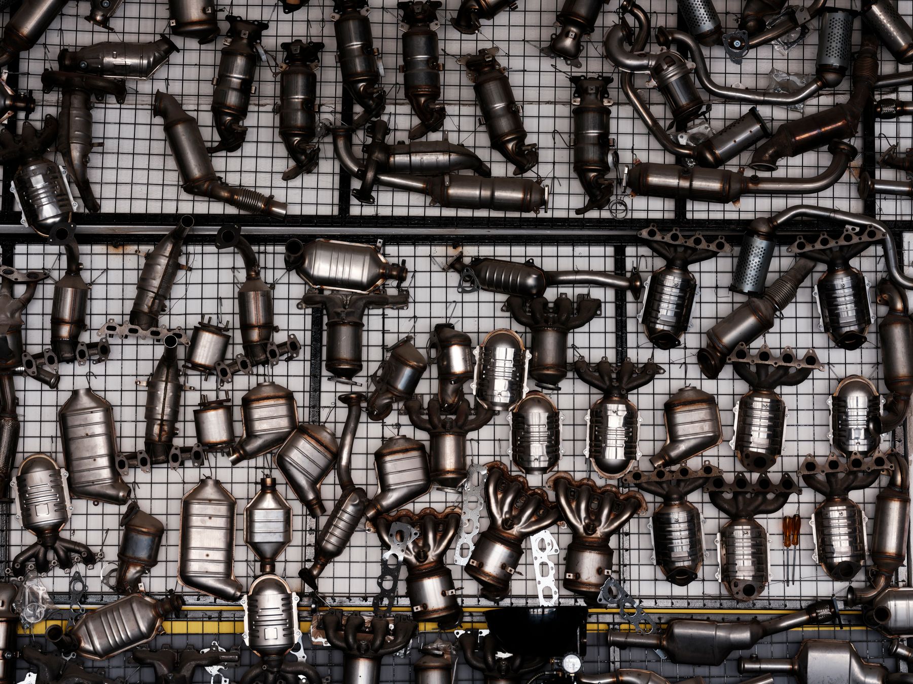 Parede de estoque com dezenas de conversores catalíticos e tubos de escapamento pendurados em uma oficina industrial